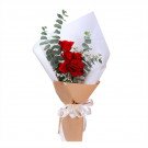 Red roses and eucalyptus in a brown paper bouquet with a white ribbon.