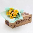 Sunshine Bouquet with yellow gerberas and peach roses in light blue wrapping, on a cardboard box.