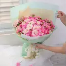 A large bouquet of pink roses and carnations wrapped in mint green paper and tied with a cream ribbon.