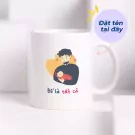 White mug with cartoon dad holding baby and Vietnamese text "Bố là tất cả" (Dad is everything).