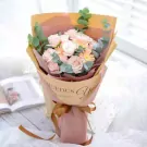 Pink roses and gerbera daisies bouquet with eucalyptus, wrapped in kraft paper with text.