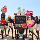 Birthday celebration on the beach with a group of smiling African men holding balloons and a "Happy Birthday Claudia" sign.