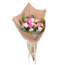 Bouquet of pink and white roses and carnations in brown wrapping with a cream ribbon.