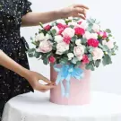 Pink box of roses, carnations, and eucalyptus, tied with a blue ribbon.