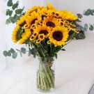 A vase overflowing with sunflowers and smaller yellow flowers, accented with eucalyptus leaves.