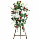 Standing funeral spray of white lilies, hydrangeas, chrysanthemums, and red roses on a wooden easel.
