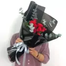 Bouquet of red roses in black paper wrap with silver ribbon, held by a person.