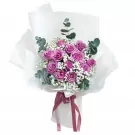 Bouquet of purple roses and baby's breath flowers wrapped in white paper.