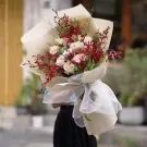Bouquet of pink roses, red cymbidium orchids, and greenery, wrapped in cream paper and white tulle.