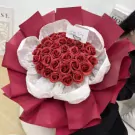 A bouquet of red roses, artfully arranged with white and deep red wrapping.