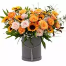 A bouquet of sunflowers and orange and pink roses in a grey box with tassel detail.