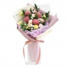 Bouquet of pink chrysanthemums, cream roses, yellow carnations, and greenery in purple and cream paper.