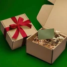 Two cardboard gift boxes, one wrapped with red ribbon, the other open with straw and dried flowers.