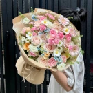 Bouquet of pink and white roses, daisies, and carnations, wrapped in brown paper.