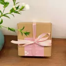 A brown gift box with pink ribbon and a pink label saying "the beauty around you and be happy".