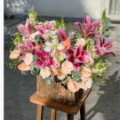 Pink lilies, roses, and anthuriums in a rustic wooden box on a stool.