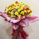 Bright yellow roses and orange gerbera daisies in a large pink floral arrangement.
