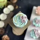Cupcake with teal frosting, purple roses, and gold sprinkles on a stand.