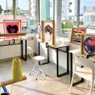 Punch needle workshop with colorful yarn, art pieces, and chairs in a bright room.