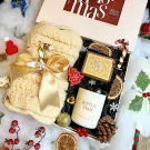 Christmas gift box with knitted scarf, candle, music box, dried oranges, pinecone, and festive ornaments.