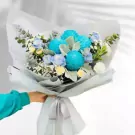 Hand holding a bouquet of blue and white flowers, including chrysanthemums and roses.