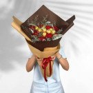 Chocolate and red carnation bouquet wrapped in brown paper, held by a person.