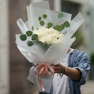 Bouquet of white roses and eucalyptus leaves wrapped in white paper with a pink ribbon.