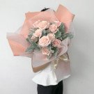 A bouquet of pink roses with dusty miller and pale pink wrapping, tied with a cream ribbon.