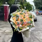 A person holds a large bouquet of orange and pink roses, lisianthus, and tanacetum daisies.