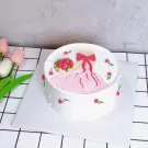 White cake with pink frosting of a girl holding flowers and wearing a dress.
