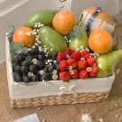 Fruit basket with mangoes, pears, oranges, strawberries, grapes, and small white flowers.