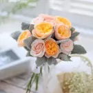 A bouquet of peach, pink, and yellow roses with dusty green foliage.