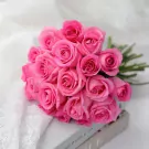 A bouquet of 20 bright pink roses with water droplets, resting on a lace cloth and a book.
