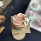 Pink rose cupcake with white flowers and gold flakes, on a stand.