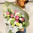 A bouquet of pink lotus flowers, green lotus seed pods, and white carnations wrapped in green paper.