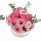 Pink gerbera daisies, carnations, and roses in a clear glass vase with eucalyptus.