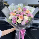 A large bouquet of purple and pink roses, gerbera daisies, and other flowers.