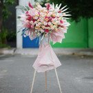 A tall flower arrangement with pink and orange roses, on a wooden easel.