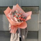 A bouquet of peach roses and grey leaves wrapped in peach and white paper.