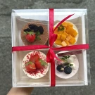 A gift box of four mini cakes: tiramisu, mango, strawberry, and blueberry desserts.