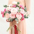 Bridal bouquet with pink roses, gerbera daisies, carnations, and eucalyptus, held by a person in a peach dress.
