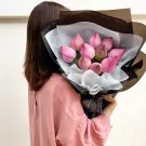Woman in pink shirt holding a bouquet of pink lotus flowers wrapped in black and white paper.