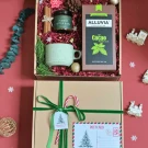 Christmas gift box with cocoa powder, mug, candle, cinnamon sticks, and festive decorations.