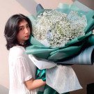 A young woman in a white shirt holds a large bouquet of white flowers.