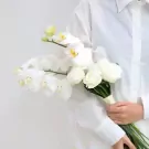 White orchid and rose bridal bouquet held by a person in a white shirt.
