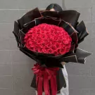 A large bouquet of 99 red roses wrapped in black paper with a red bow.