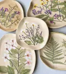 Ceramic plates with pressed flowers and leaves, including ferns and daisies.