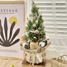 Decorated pine tree with pinecones, gifts, and bows in a burlap pot.