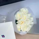 Bouquet of white roses wrapped in white paper, with a white envelope in the foreground.