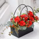 Black bag arrangement with red roses, berries, thistle, and greenery.